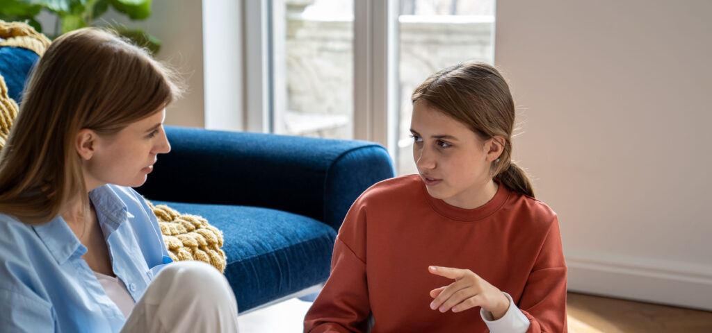 Mother and teenage daughter sitting on the floor in their living room, talking about vaping
